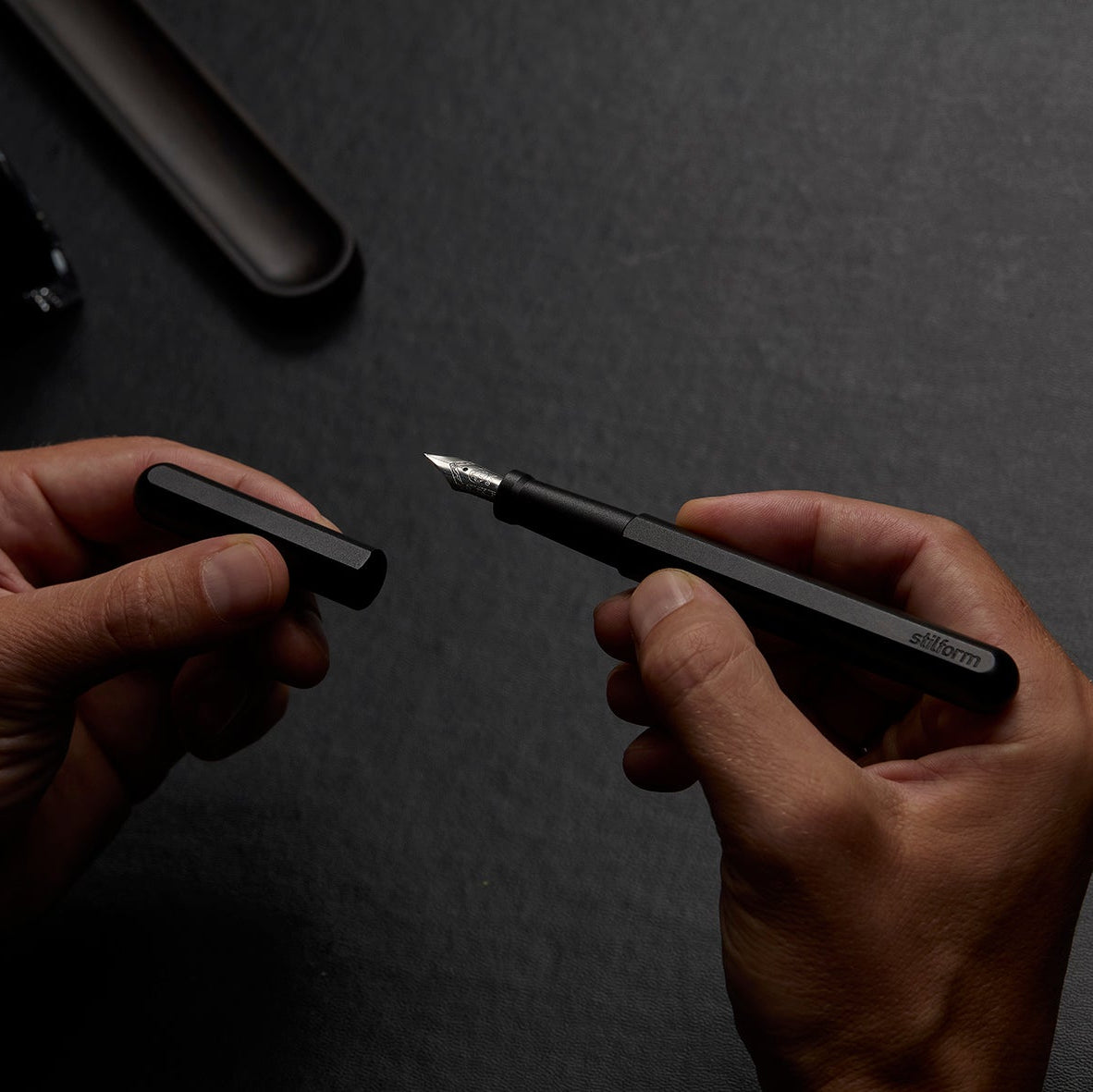 Füllfederhalter Ink Warp Black mit Stahlfeder in der Hand beim Abziehen der Kappe