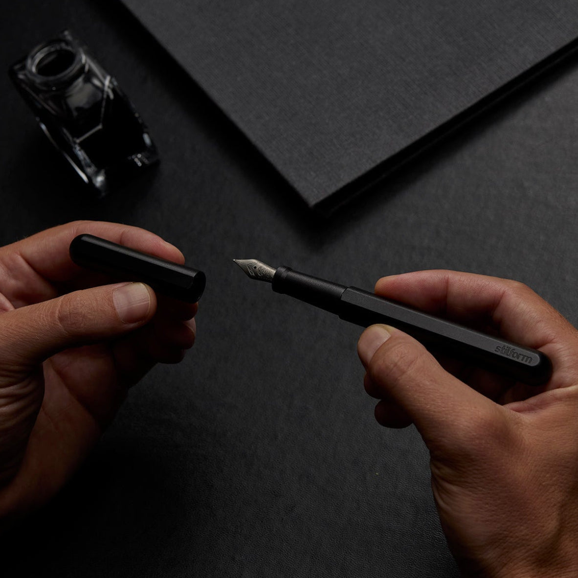 Füllfederhalter Ink Warp Black mit Titanfeder in der Hand beim Abziehen der Kappe