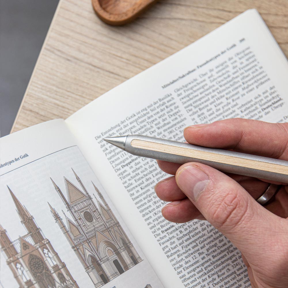 AEON Magnesium Bleistift mit Eternal-Spitze, gehalten in der Hand über einem aufgeschlagenen Buch